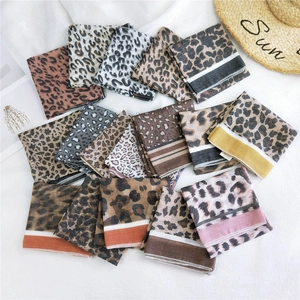 Multiple stylish leopard print cotton linen scarves displayed with a straw hat on white fabric
