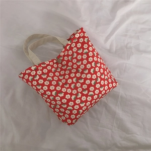 Detailed close-up of red floral tote bag featuring white daisies and a metal snap button