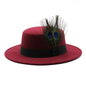 Detail of a wine red wool boater hat featuring natural peacock feathers and black ribbon