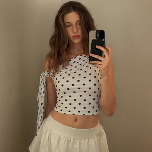 Close-up of white one-shoulder polka dot top with tie detail and pleated mini skirt