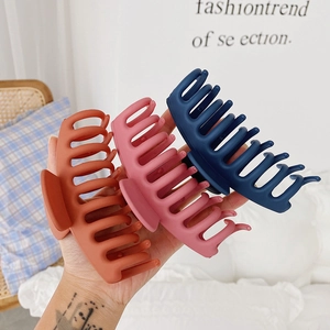 Three large matte hair claws in orange, pink, and navy blue shown held in hand