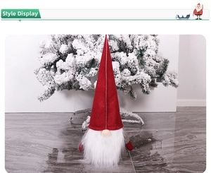 Detail of red felt Christmas gnome with white beard and snowy pine tree background