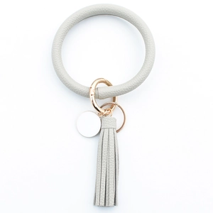 Detail of light grey faux leather keychain bracelet with golden metal ring and tassel charm