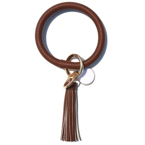 Macro detail of brown leather keychain with gold ring, tassel, and round white pendant