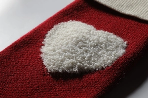 Detail shot of a red knitted Christmas stocking featuring a 3D white looped heart pattern