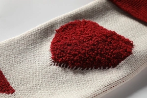 Close-up of beige knitted Christmas stocking with 3D red loop yarn heart embroidery