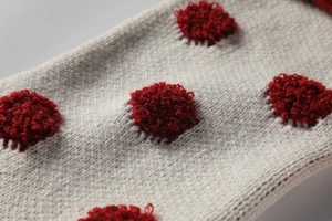 Gros plan du tissu tricoté beige avec pois rouges en 3D pour chaussette de Noël