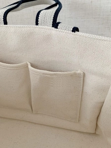 Detail view of beige canvas tote interior featuring two slip pockets and blue woven edges