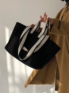 Detail of a black canvas tote bag with beige woven handles held by a model in soft light