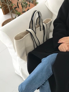 Detail of a large cream canvas tote bag with black striped handles on a white sofa