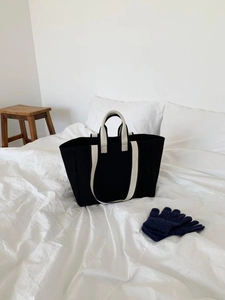 Close-up of a minimalist black canvas tote bag with beige straps on a white fabric surface