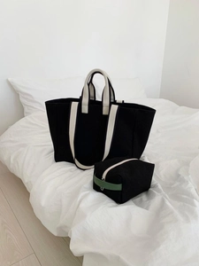 Detail of a black canvas tote bag set with contrast straps on white bedding