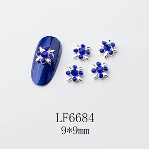 Détail macro de charmes d'ongles fleurs argentées 9x9mm avec strass bleus et perles