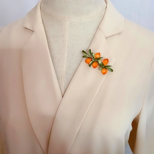 Detail of orange berry brooch pinned on a beige blazer lapel for retro botanical style