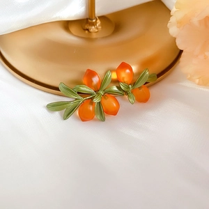 Macro shot of orange glass berry earrings with green leaves on white silk fabric