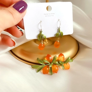 Detailed set of orange berry glass brooch and 925 silver earrings on white silk fabric