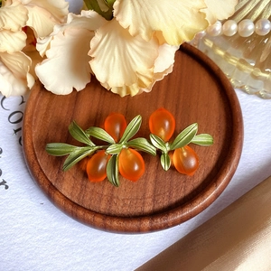 Close-up of frosted orange glass berry brooch with green metal leaves on wood