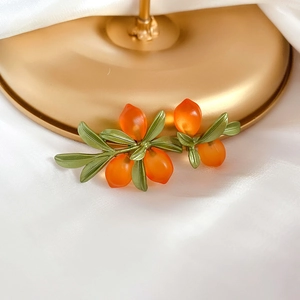 Vintage orange glaze berry brooch with green leaves on white silk and gold stand
