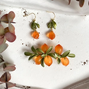 Vintage orange glass berry brooch and earrings set with green metal leaves on a white surface