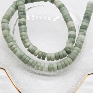 Green and white natural stone heishi disc beads on a gold-rimmed glass plate