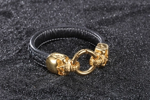 Detail of black leather bracelet with golden skull accents on dark gravel