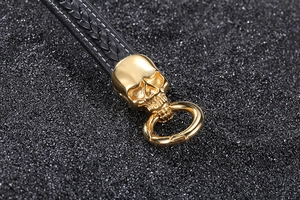 Macro view of a gold skull charm on a black braided leather motorcycle bracelet