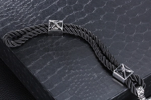 Detail of black braided rope bracelet with silver textured metal cubes on leather
