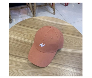 Détail d'une casquette corail avec lettre N blanche brodée sur une table en bois
