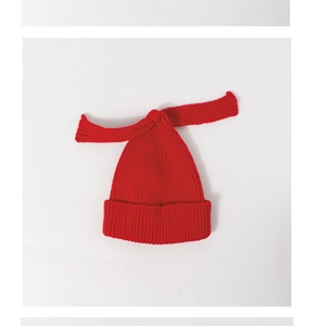 Close-up of red knit baby hat with decorative long ribbons on a plain white background