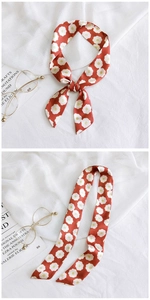Floral print narrow silk scarf in orange red tied on a bag handle as a decorative accessory