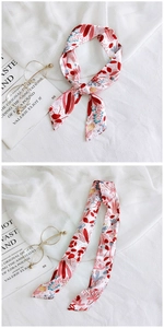Detail of pink floral twilly silk scarf tied in a bow on soft white fabric background