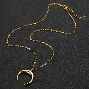 Close-up of golden crescent moon pendant with fine chain on dark background