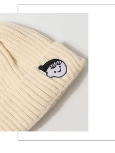 Close-up of cream knit beanie with ribbed texture and cartoon portrait embroidery