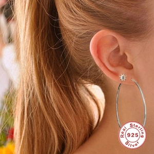 Close-up of 925 sterling silver sun stud and large hoop earring on female ear