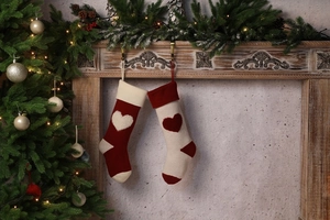 Close-up of knitted Christmas stockings with 3D heart patterns hanging on a fireplace