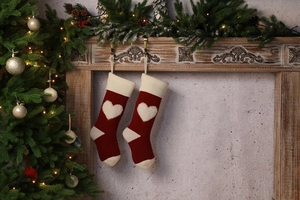 Close-up of knitted red Christmas stockings with white 3D heart on a cozy wooden fireplace