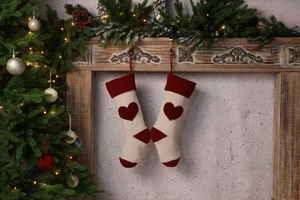 Close-up of beige knitted Christmas stockings with 3D red heart hanging on a fireplace