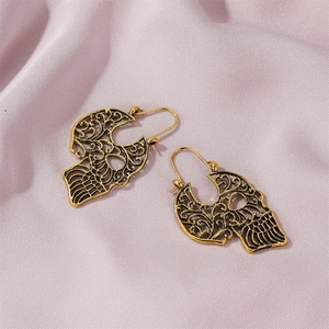 Detail of gold hollowed skull earrings featuring intricate Gothic carving on pink fabric
