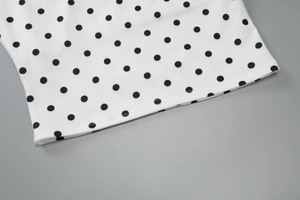 Close-up of black polka dot fabric on white top showing detailed hem stitching quality