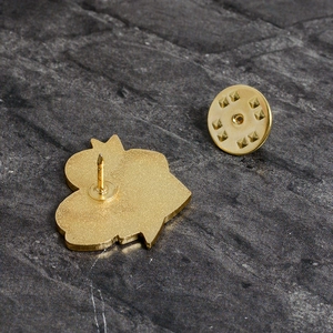 Golden metal heart brooch with butterfly clutch pin back on a dark stone background