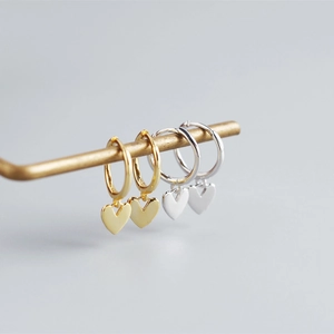 Macro detail of heart charm hoop earrings in gold and silver finish on display