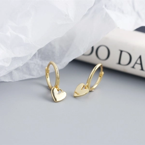 Close-up of elegant gold heart-shaped charm hoop earrings on white texture background