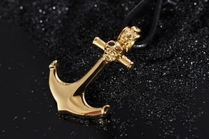 Macro shot of gold skull anchor pendant with black braided rope on a dark sand background