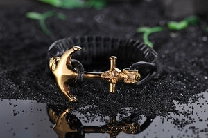 Close-up of golden anchor clasp on black braided leather bracelet over dark sand stones
