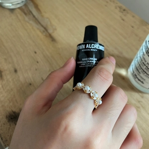 Detail of a gold floral ring with pearls and crystals worn on a hand over a wooden table