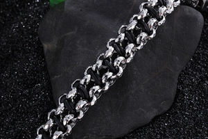 Macro shot of silver stainless steel chain linked with black braided leather on dark rocks