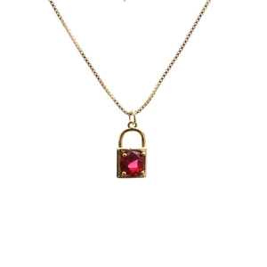 Close-up of golden necklace featuring a micro-pave padlock pendant with a red gemstone