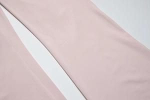 Detailed close-up of light pink flare pants fabric with fine texture and smooth drape