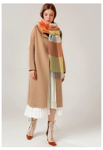 Detail of warm-toned plaid scarf with tassels styled over a camel wool coat and skirt