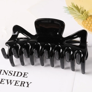 Detail of a large black glossy hair claw clip with a hollow geometric design on white paper